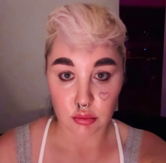 Person with short blonde hair and septum piercing, appearing serious in a dimly lit room discussing Amanda Bynes claim viral.