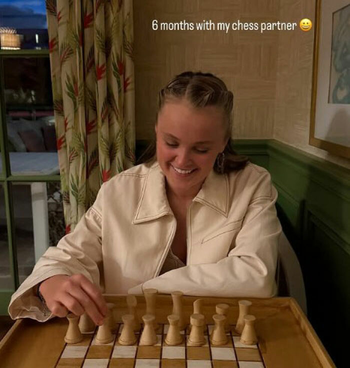 Young woman smiling and playing chess, illustrating JoJo Siwa's fans stunned and confused after Chris Hughes' reality TV confession.