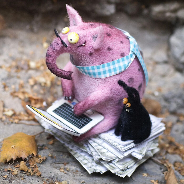 Adorably strange handmade creatures toy in purple with yellow eyes using a laptop next to a small black creature.