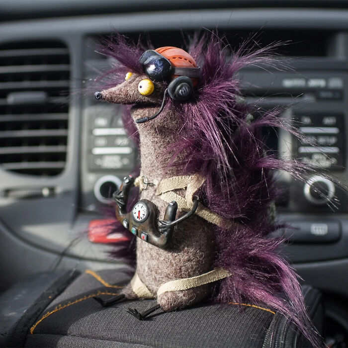 Handmade creature toy with purple fur and headset sitting inside a car, showcasing adorably strange handmade creatures.