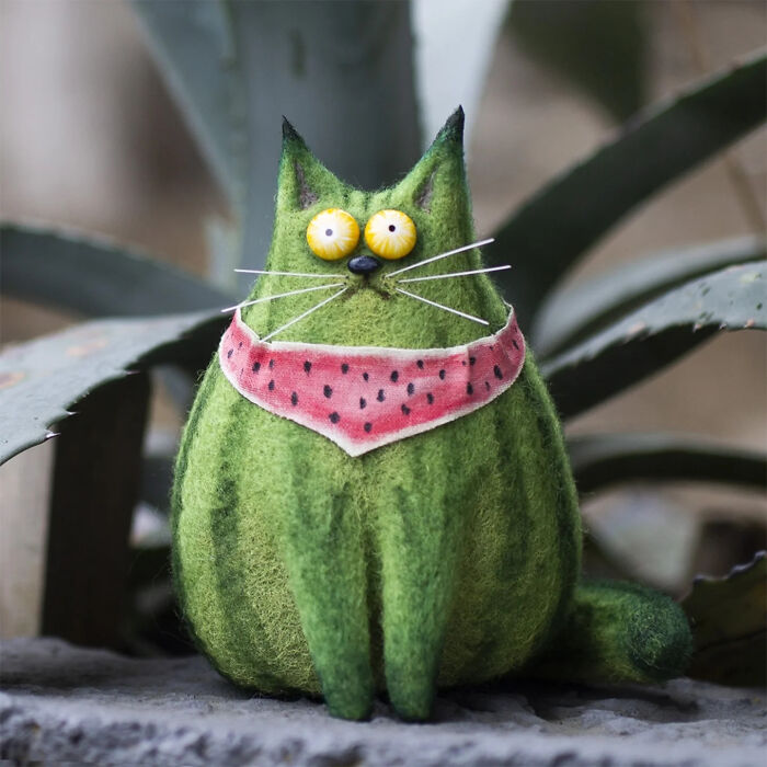 Handmade creature toy resembling a green cat with yellow eyes and a pink scarf, showcasing adorably strange design.