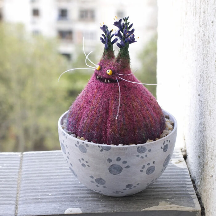 Handmade creature toy with purple wool texture, yellow eyes, and plant-like antennae in a paw print pot.