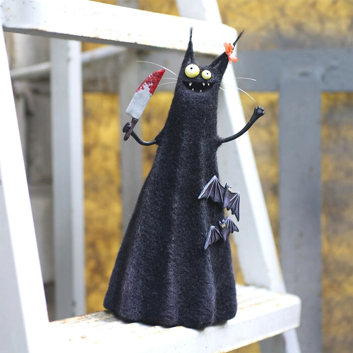 Handmade creature toy with wide eyes holding a bloodstained knife and small bats attached to its black felt body.