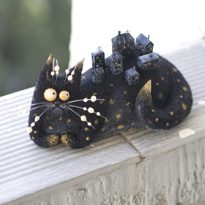 Handmade creature toy shaped like a black cat with miniature buildings on its back, showcasing adorably strange art design.