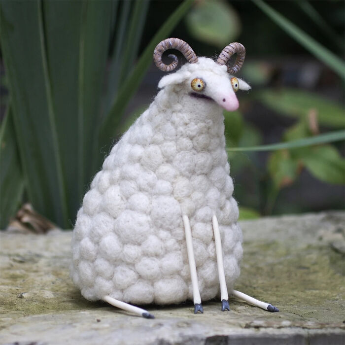 Handmade creature toy with curly horns and textured white wool sitting outdoors on a stone surface.
