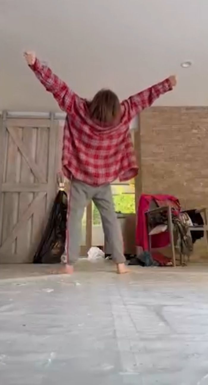 Taryn Manning in a red plaid shirt and gray pants with arms raised indoors, fans worried after bizarre video.