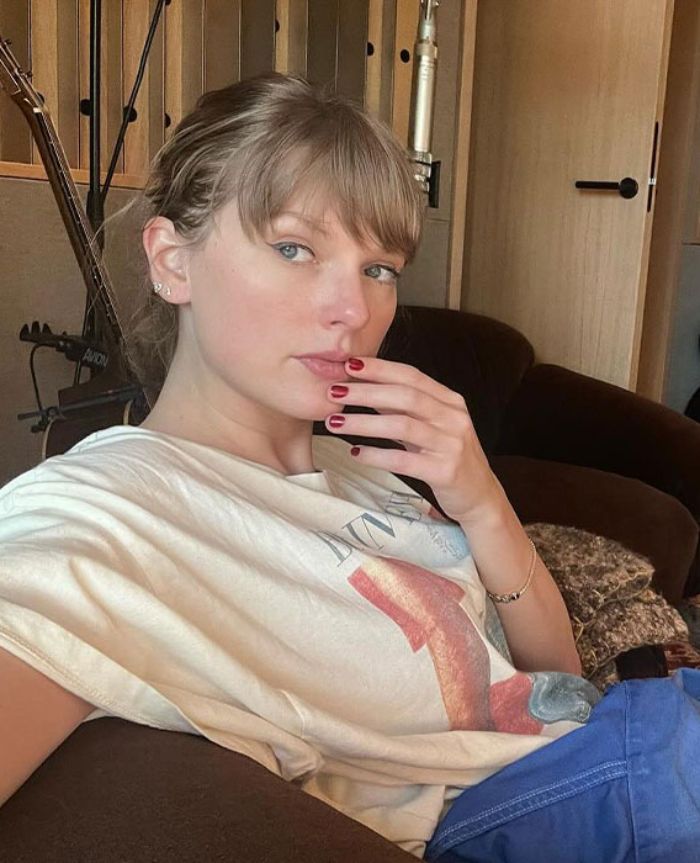 Taylor Swift sitting casually indoors with hand near face, linked to an embarrassing video sparking debate about her manners.
