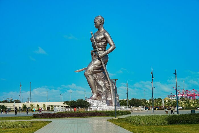 Large spectacular sculpture of a woman holding a spear and sword in an open plaza under a clear blue sky.