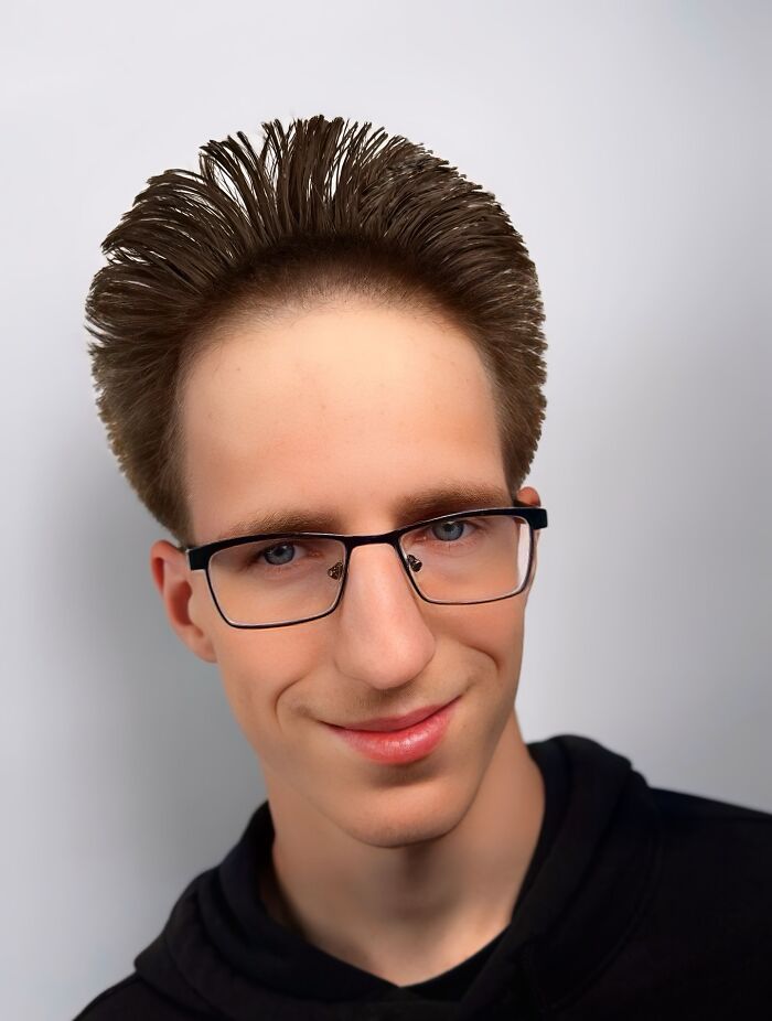 Young man with bold barber haircut styled upwards, wearing glasses and a black hoodie against a plain background