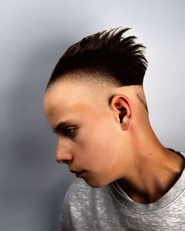 Side profile of a young man with a bold barber haircut featuring a high fade and textured top hairstyle.