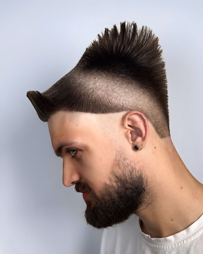 Side profile of man with bold barber haircut featuring a high fade and spiked mohawk hairstyle against a plain background.
