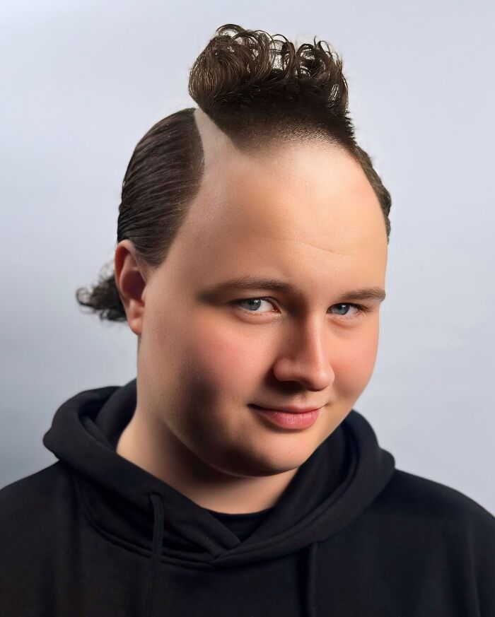 Young man with bold barber haircut featuring shaved sides and curly hair on top, wearing a black hoodie against a neutral background.