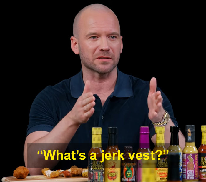 Man in navy shirt gesturing with hands during interview, surrounded by hot sauce bottles, discussing viral Hollywood blunder.