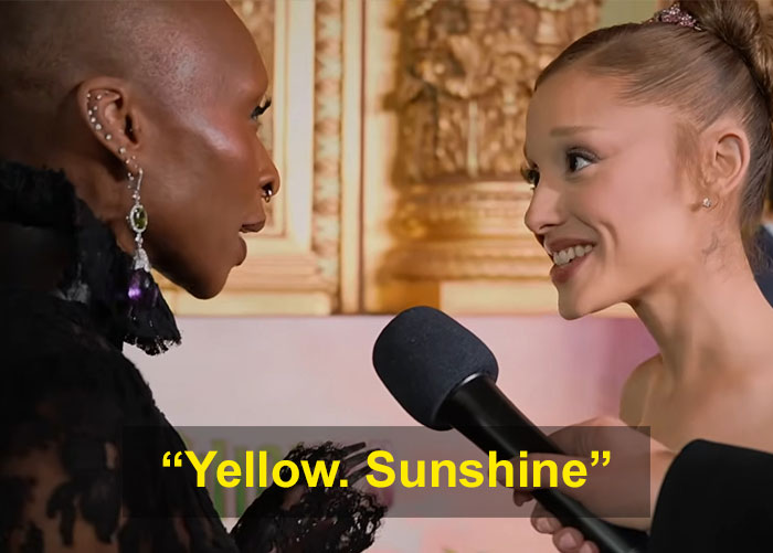 Cynthia Erivo and Ariana Grande in a close, intense interaction during an interview with a microphone between them.