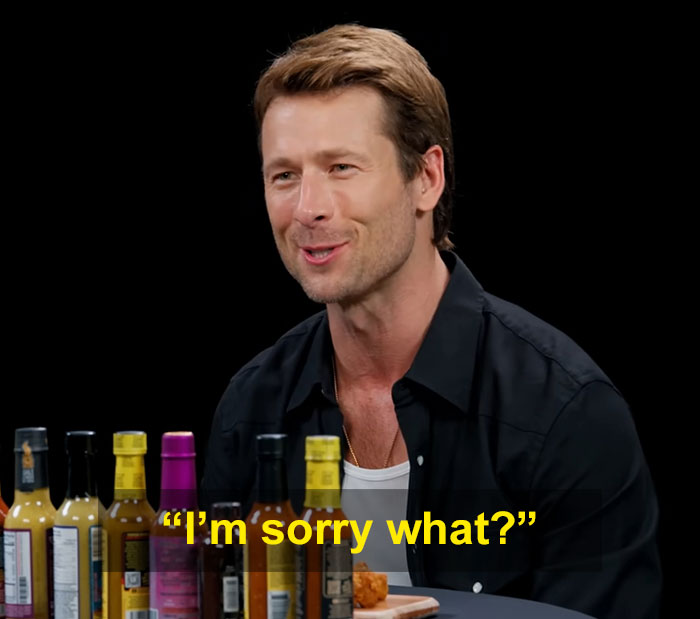 Glen Powell during an interview with various hot sauce bottles, highlighting a viral Hollywood blunder moment.