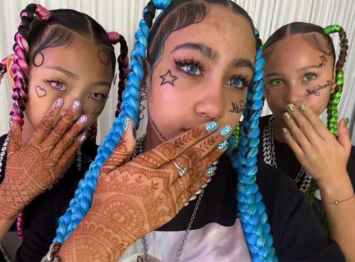 Three young girls with colorful braids, face tattoos, and henna designs highlighting celebrity parenting styles debate.