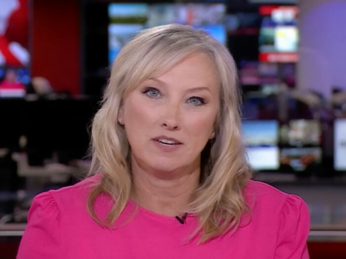 BBC anchor in newsroom wearing pink top discussing discipline for showing disgust on-air related to trans people remarks.