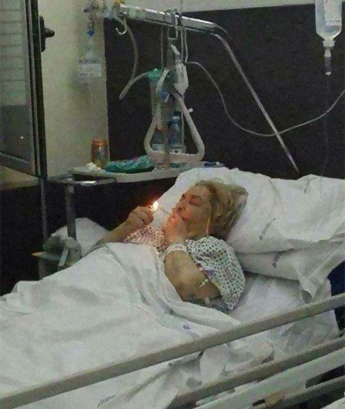 Patient in hospital bed lighting a cigarette, a striking frozen frame capturing an unexpected moment of defiance.