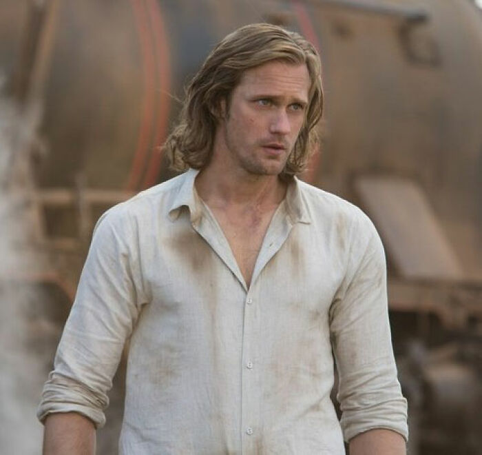 Alexander Skarsg&aring;rd with a rugged, dirty white shirt and long hair, showing a unique detail in his perfect man look.
