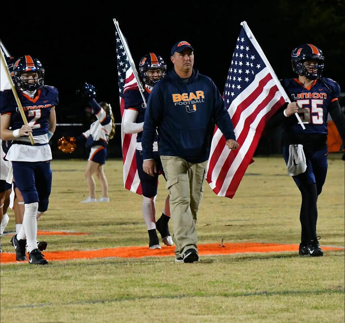 Football coach walking on field with players holding American flags, highlighting missing football coach case mystery. Football coach walking on field with players holding American flags, highlighting missing football coach case mystery.