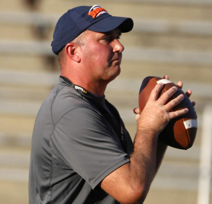 Football coach in cap holding a football, focused during practice, related to missing coach mystery case. Football coach in cap holding a football, focused during practice, related to missing coach mystery case.