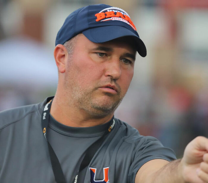 Man wearing a blue cap and gray shirt, focused and pointing, related to missing football coach case mystery. Man wearing a blue cap and gray shirt, focused and pointing, related to missing football coach case mystery.