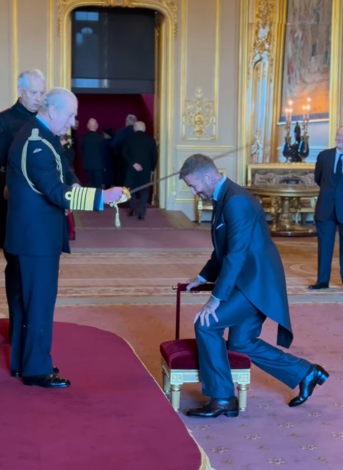 David Beckham kneeling in a formal ceremony as he receives his sir title in an ornate royal setting. David Beckham kneeling in a formal ceremony as he receives his sir title in an ornate royal setting.