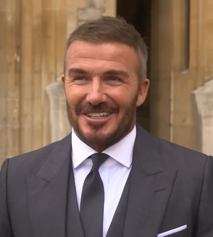 David Beckham in a formal suit smiling outside a historic building after receiving the Sir title and new name announcement David Beckham in a formal suit smiling outside a historic building after receiving the Sir title and new name announcement