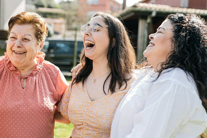 Three women laughing together outdoors, sharing moments that reveal unusual childhood habits and memories.