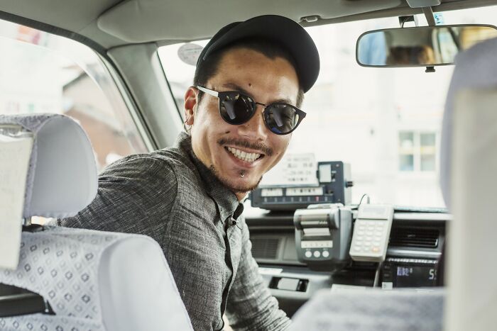 Man wearing sunglasses and a cap smiling inside a taxi, illustrating the craziest coincidences people experienced.