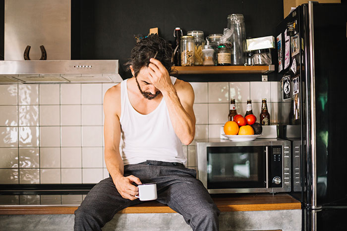 Grieving dad sitting in kitchen, holding a cup, looking distressed while trying to make daughter&rsquo;s birthday special.