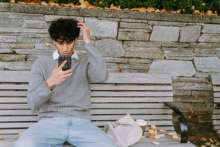 Young man on a bench looking frustrated while using phone, symbolizing caretaker snapping after guilt trips and sacrifice.