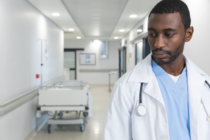 Male doctor in hospital corridor looking down thoughtfully, reflecting on eerie patient encounters that still haunt doctors.