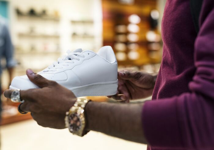 Customer holding a white sneaker inside a store likely preparing for Black Friday shopping rush.