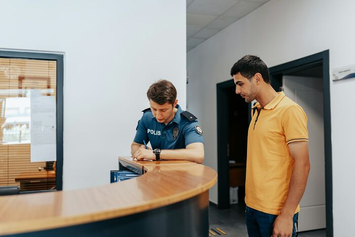 Police officer in uniform assisting a man at a reception desk, illustrating comically absurd facts about everyday situations.