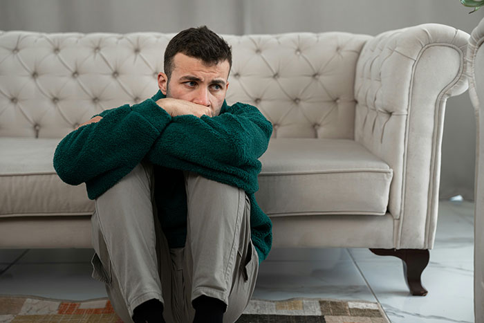 Young man sitting on floor, looking upset and thoughtful, reflecting on toxic girlfriend and relationship ultimatum.