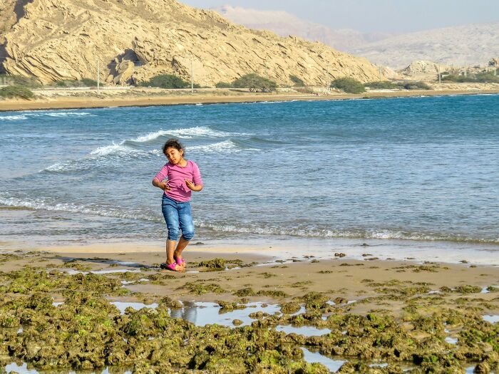 Child wearing pink and blue acting weird on a rocky beach, showing quirky behavior clearly passed down from parents