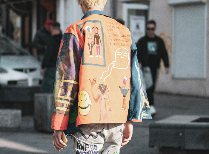 Person wearing colorful painted jacket and jeans in an urban setting, showcasing unique American street fashion style.