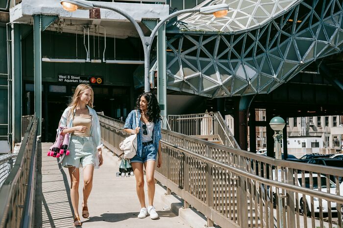 Two women walking and talking near NY Aquarium Station, enjoying a sunny day in the US urban environment.