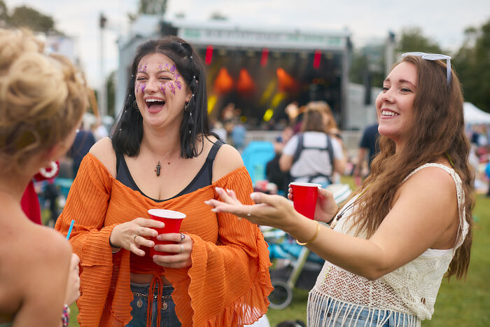 Three women enjoying an outdoor festival in the US, laughing and holding red cups in a lively social gathering.