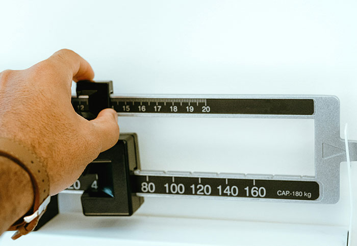 Hand adjusting a mechanical scale showing weight in kilograms, representing American expats noticing differences in Canada.