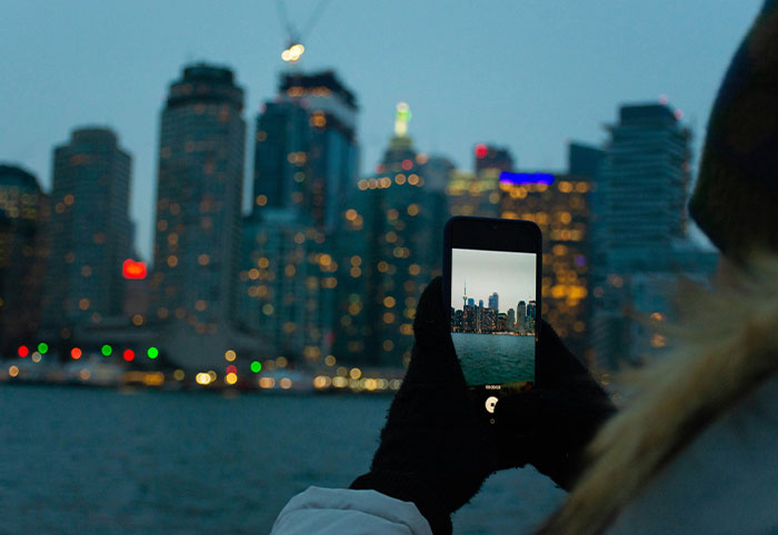 Person wearing gloves photographing a Canadian city skyline at dusk, illustrating American expats noticing cultural differences.