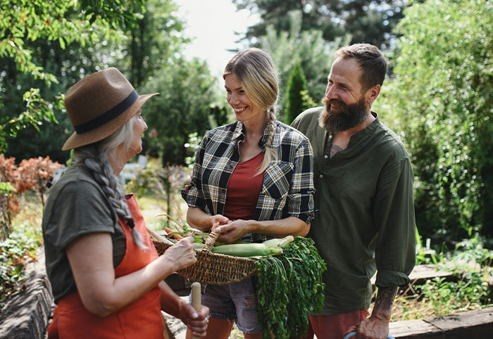 American expats interacting with a local gardener while holding fresh vegetables in a lush Canadian garden.