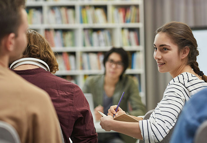Young woman speaking and taking notes in a casual group setting, illustrating American expats noticing cultural differences in Canada.
