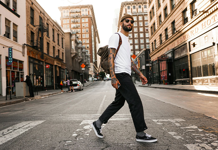 Young American expat with tattoos and backpack walking in an urban setting, observing cultural differences in Canada.