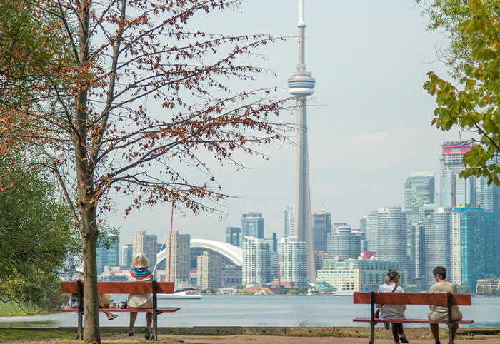 People sitting on benches by a lake overlooking the Toronto skyline, illustrating American expats in Canada observations.