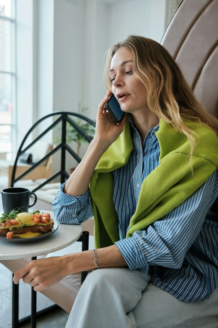 Woman talking on phone at cafe table with breakfast and coffee, illustrating crazy coincidences people experienced