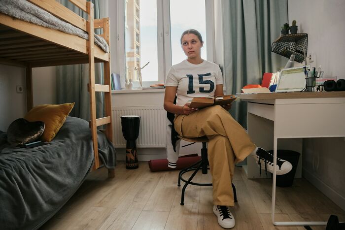 Teen girl in a bedroom holding a book, reflecting on parenting challenges and ways parents fail at raising kids.