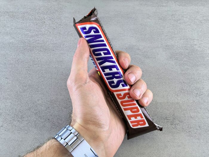 Hand holding a Snickers Super chocolate bar, illustrating lovable things clueless dads did during pregnancy.