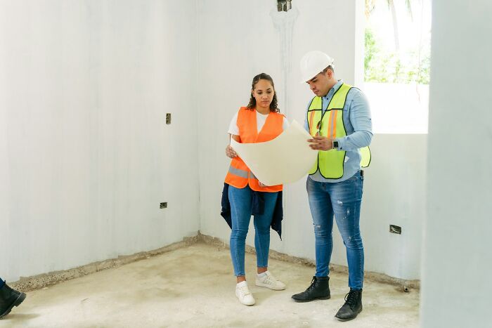 Two construction workers in safety vests reviewing plans inside an unfinished room, illustrating family roles and golden child dynamics.